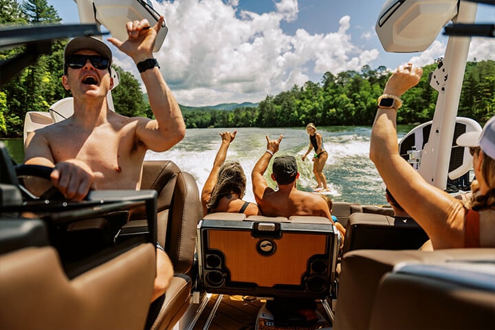 Friends cheer on a rider wakesurfing behind a 2025 Malibu Wakesetter 23 LSV in the sunshine