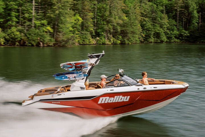 A red, white, and black All-New 2025 Malibu M230 cruising down the lake in the sunshine