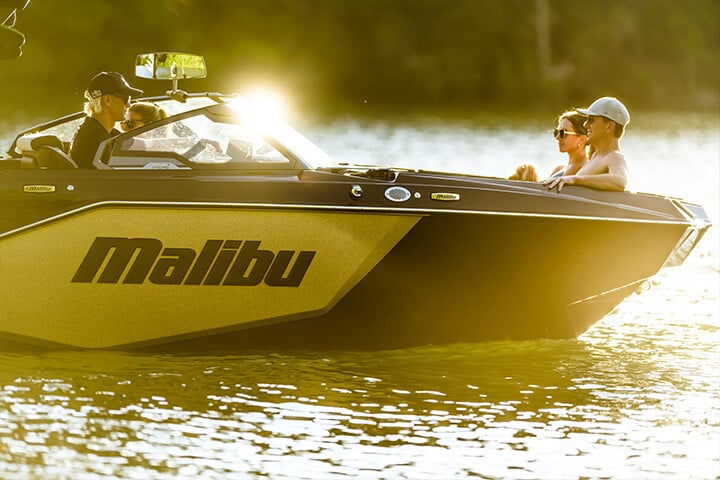 The sunset shining on a black and gold 2025 Malibu M242 with people relaxing